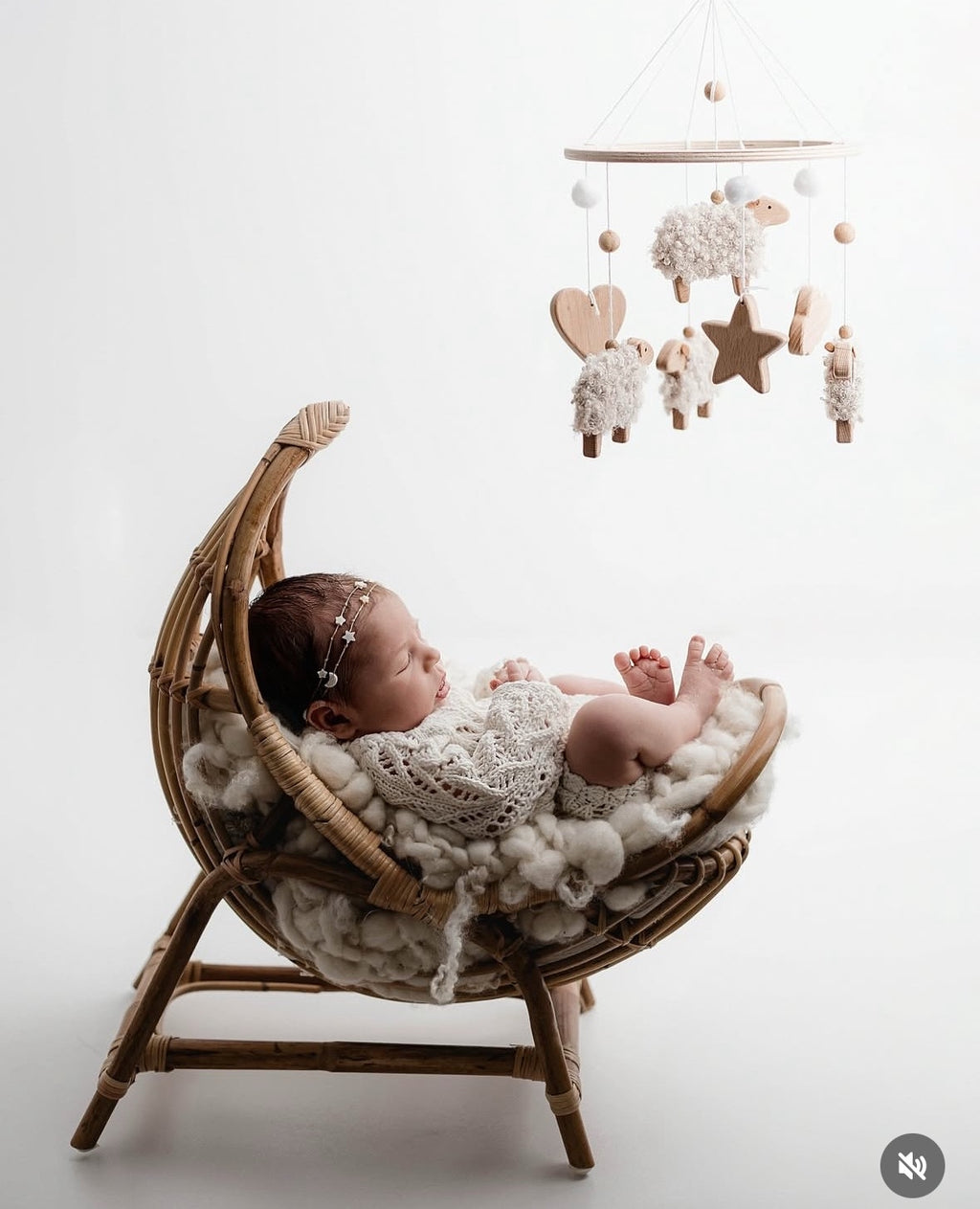 Newborn baby in a wicker basket with a mobile above, on a white background