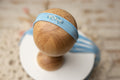 A blue and beige newborn headband displayed on a wooden stand, with a floral pattern on the fabric and a small bead embellishment.