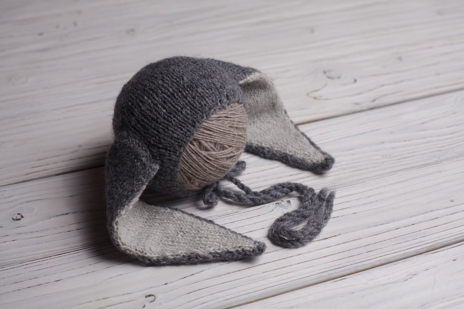 A gray newborn knit sleep hat with a pom-pom lying on a wooden surface.
