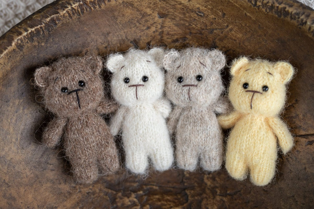 A set of three crochet teddy bear toys in beige, brown, and yellow colors placed on a wooden surface, with a background that is out of focus.