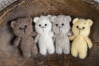 A set of three crochet teddy bear toys in beige, brown, and yellow colors placed on a wooden surface, with a background that is out of focus.
