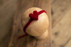 A wooden newborn headband with a red bow on a wooden surface.