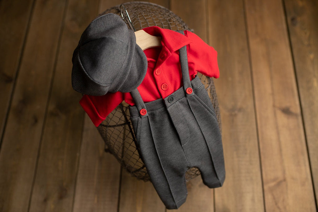 A newborn boy romper with suspenders and a stylish hat placed on a wooden surface.