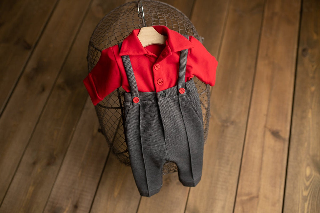 A newborn boy romper with suspenders and a stylish hat placed on a wooden surface.
