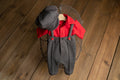 A newborn boy romper with suspenders and a stylish hat placed on a wooden surface.