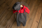 A newborn boy romper with suspenders and a stylish hat placed on a wooden surface.