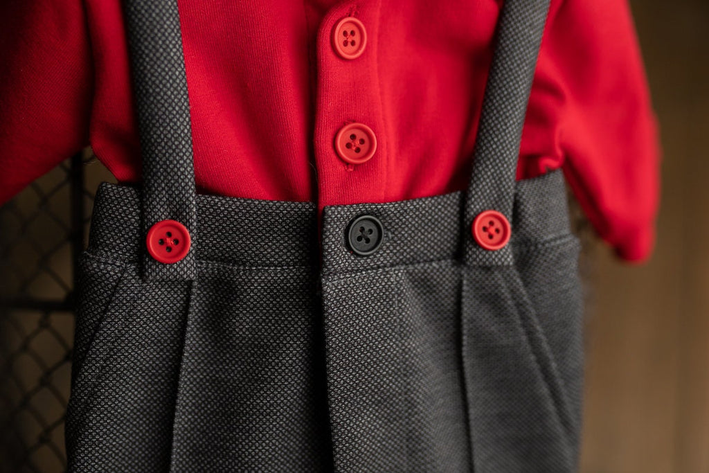 A newborn boy romper with suspenders and a stylish hat placed on a wooden surface.