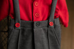 A newborn boy romper with suspenders and a stylish hat placed on a wooden surface.