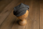 A newborn boy romper with suspenders and a stylish hat placed on a wooden surface.