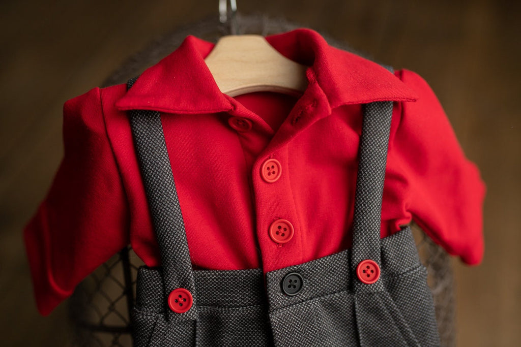 A newborn boy romper with suspenders and a stylish hat placed on a wooden surface.