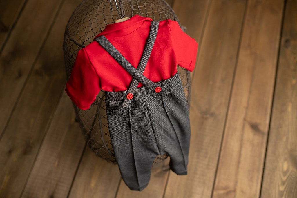 A newborn boy romper with suspenders and a stylish hat placed on a wooden surface.