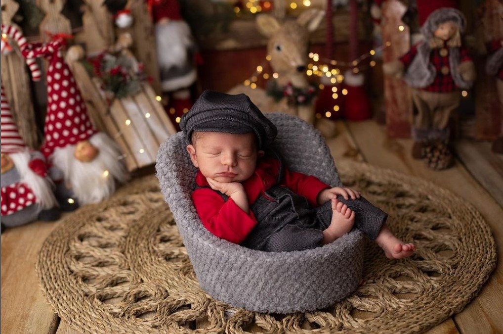 A newborn boy romper with suspenders and a stylish hat placed on a wooden surface.